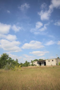 Terk edilmiş bir yerleşkenin depoları güneşli bir günde ağaçlarla çevrili İtalya kırsalında kuru çimenler ve çakıllarla çevrili bir bahçeden görülebiliyor.