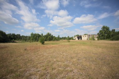 Terk edilmiş bir yerleşkenin depoları güneşli bir günde ağaçlarla çevrili İtalya kırsalında kuru çimenler ve çakıllarla çevrili bir bahçeden görülebiliyor.