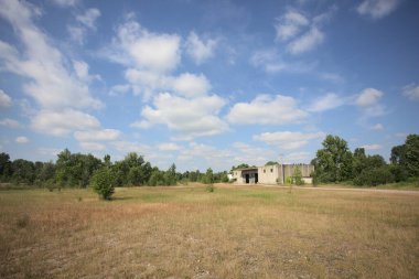 Terk edilmiş bir yerleşkenin depoları güneşli bir günde ağaçlarla çevrili İtalya kırsalında kuru çimenler ve çakıllarla çevrili bir bahçeden görülebiliyor.