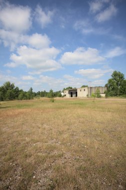 Terk edilmiş bir yerleşkenin depoları güneşli bir günde ağaçlarla çevrili İtalya kırsalında kuru çimenler ve çakıllarla çevrili bir bahçeden görülebiliyor.