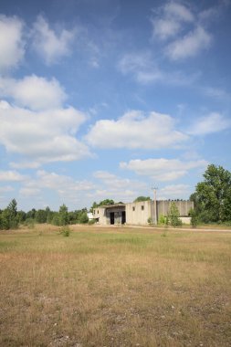 Terk edilmiş bir yerleşkenin depoları güneşli bir günde ağaçlarla çevrili İtalya kırsalında kuru çimenler ve çakıllarla çevrili bir bahçeden görülebiliyor.