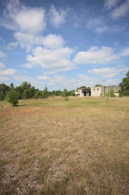 Terk edilmiş bir yerleşkenin depoları güneşli bir günde ağaçlarla çevrili İtalya kırsalında kuru çimenler ve çakıllarla çevrili bir bahçeden görülebiliyor.