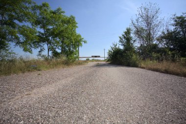 Eskimiş asfalt yollar, güneşli bir günde ağaçların çerçevelediği paslı bir bar tarafından kapatılmış.