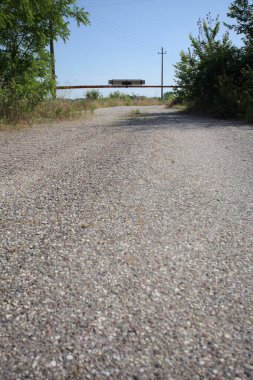 Eskimiş asfalt yollar, güneşli bir günde ağaçların çerçevelediği paslı bir bar tarafından kapatılmış.