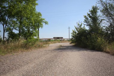 Eskimiş asfalt yollar, güneşli bir günde ağaçların çerçevelediği paslı bir bar tarafından kapatılmış.