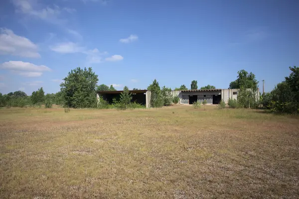 Terk edilmiş bir yerleşkenin depoları güneşli bir günde ağaçlarla çevrili İtalya kırsalında kuru çimenler ve çakıllarla çevrili bir bahçeden görülebiliyor.