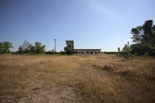 Çalıların yanındaki terk edilmiş bina ve güneşli bir günde çıplak bir avludan görülen elektrik hattı.
