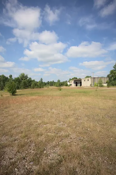 Terk edilmiş bir yerleşkenin depoları güneşli bir günde ağaçlarla çevrili İtalya kırsalında kuru çimenler ve çakıllarla çevrili bir bahçeden görülebiliyor.