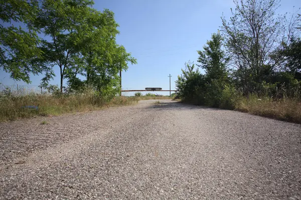 Eskimiş asfalt yollar, güneşli bir günde ağaçların çerçevelediği paslı bir bar tarafından kapatılmış.
