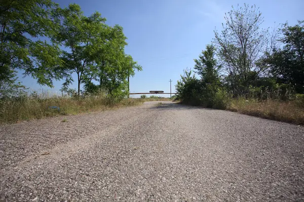 Eskimiş asfalt yollar, güneşli bir günde ağaçların çerçevelediği paslı bir bar tarafından kapatılmış.
