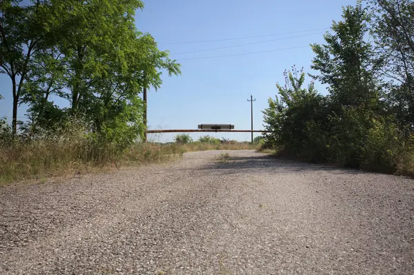 Eskimiş asfalt yollar, güneşli bir günde ağaçların çerçevelediği paslı bir bar tarafından kapatılmış.