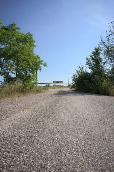 Eskimiş asfalt yollar, güneşli bir günde ağaçların çerçevelediği paslı bir bar tarafından kapatılmış.