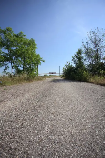 Eskimiş asfalt yollar, güneşli bir günde ağaçların çerçevelediği paslı bir bar tarafından kapatılmış.