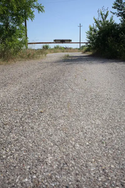 Eskimiş asfalt yollar, güneşli bir günde ağaçların çerçevelediği paslı bir bar tarafından kapatılmış.