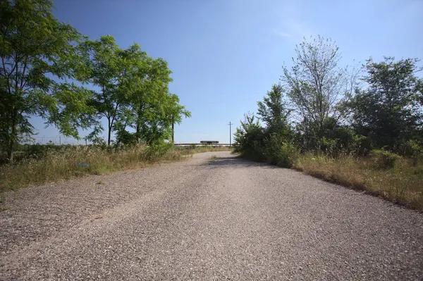 Eskimiş asfalt yollar, güneşli bir günde ağaçların çerçevelediği paslı bir bar tarafından kapatılmış.