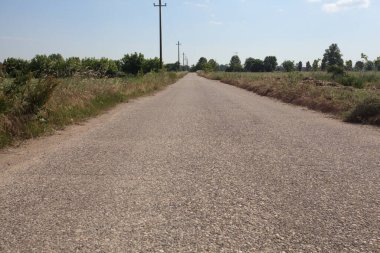 Ufuk çizgisine kadar uzanan eskimiş bir yol. İtalya kırsalında güneşli bir günde gelincikleriyle çevrili tarlalar.