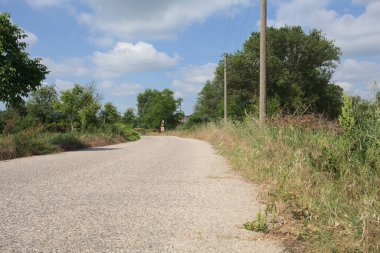 İtalya 'nın kırsal kesimlerinde güneşli bir günde bir bar tarafından engellenmiş, üzerinde elektrik hattı olan tarlalar arasındaki kirli yol.