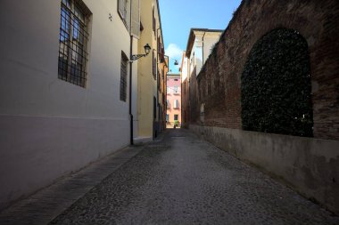 Güneşli bir günde, bir İtalyan kasabasında gölgede, kaldırımlı ve dar bir sokak.