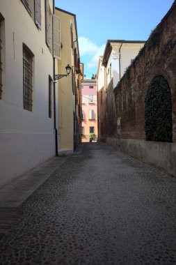 Güneşli bir günde, bir İtalyan kasabasında gölgede, kaldırımlı ve dar bir sokak.