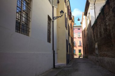 Güneşli bir günde, bir İtalyan kasabasında gölgede, kaldırımlı ve dar bir sokak.