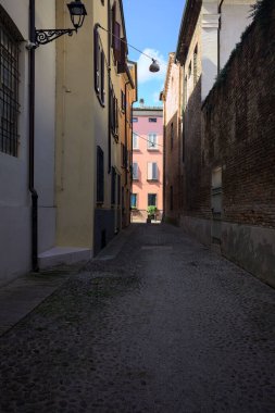 Güneşli bir günde, bir İtalyan kasabasında gölgede, kaldırımlı ve dar bir sokak.