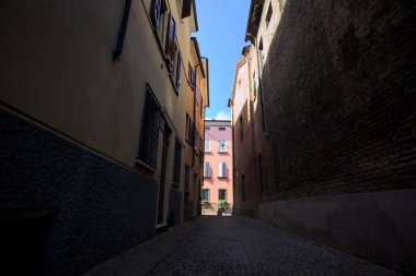 Güneşli bir günde, bir İtalyan kasabasında gölgede, kaldırımlı ve dar bir sokak.