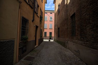 Güneşli bir günde, bir İtalyan kasabasında gölgede, kaldırımlı ve dar bir sokak.
