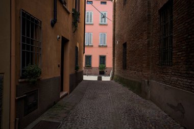 Güneşli bir günde, bir İtalyan kasabasında gölgede, kaldırımlı ve dar bir sokak.