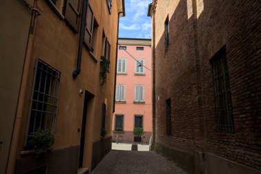 Güneşli bir günde, bir İtalyan kasabasında gölgede, kaldırımlı ve dar bir sokak.