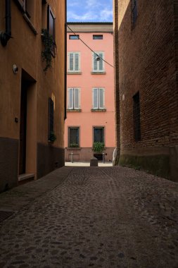 Güneşli bir günde, bir İtalyan kasabasında gölgede, kaldırımlı ve dar bir sokak.