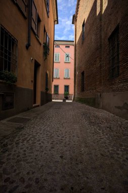 Güneşli bir günde, bir İtalyan kasabasında gölgede, kaldırımlı ve dar bir sokak.