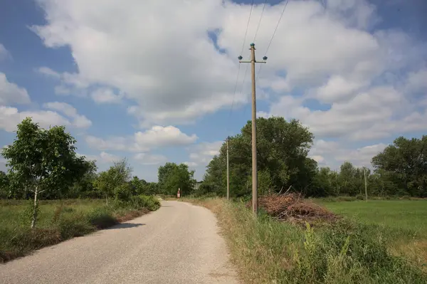 İtalya 'nın kırsal kesimlerinde güneşli bir günde bir bar tarafından engellenmiş, üzerinde elektrik hattı olan tarlalar arasındaki kirli yol.