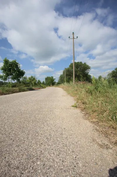 İtalya 'nın kırsal kesimlerinde güneşli bir günde bir bar tarafından engellenmiş, üzerinde elektrik hattı olan tarlalar arasındaki kirli yol.