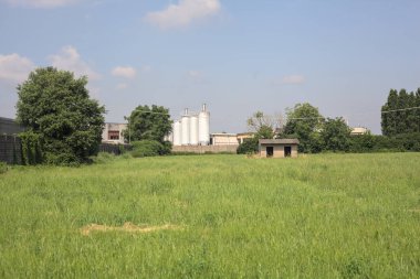 İtalya kırsalında güneşli bir günde arka planda sanayi kompleksi olan terk edilmiş beton bir kulübede terk edilmiş.