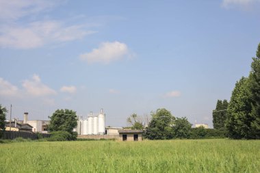 İtalya kırsalında güneşli bir günde arka planda sanayi kompleksi olan terk edilmiş beton bir kulübede terk edilmiş.