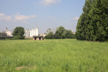 İtalya kırsalında güneşli bir günde arka planda sanayi kompleksi olan terk edilmiş beton bir kulübede terk edilmiş.