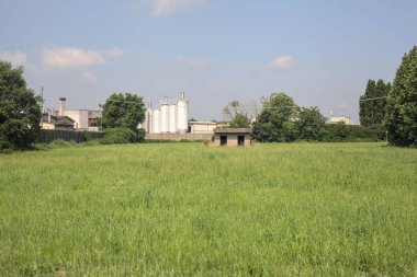 İtalya kırsalında güneşli bir günde arka planda sanayi kompleksi olan terk edilmiş beton bir kulübede terk edilmiş.