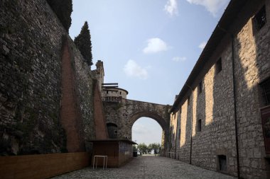 Arka planda kemer olan bir şatoda duvarla taş bina arasında bir patika var.