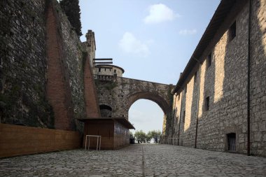 Arka planda kemer olan bir şatoda duvarla taş bina arasında bir patika var.