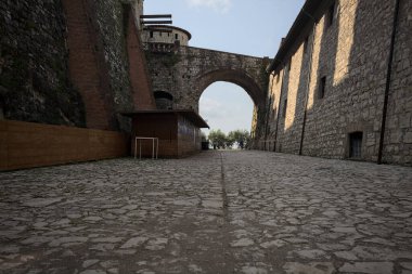 Arka planda kemer olan bir şatoda duvarla taş bina arasında bir patika var.