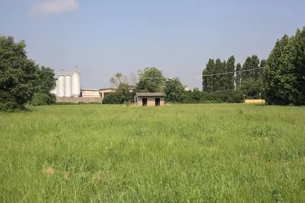 İtalya kırsalında güneşli bir günde arka planda sanayi kompleksi olan terk edilmiş beton bir kulübede terk edilmiş.