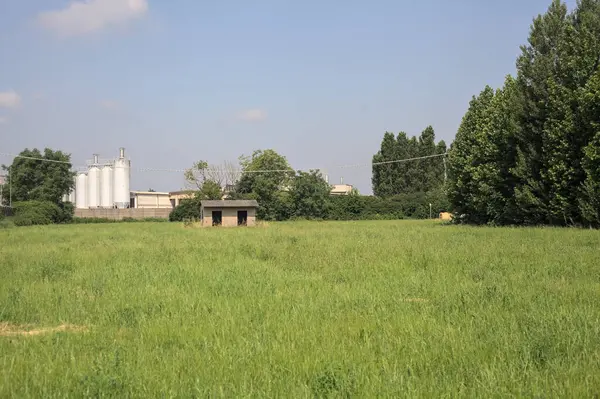 İtalya kırsalında güneşli bir günde arka planda sanayi kompleksi olan terk edilmiş beton bir kulübede terk edilmiş.