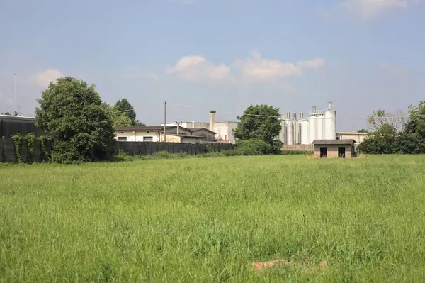 İtalya kırsalında güneşli bir günde arka planda sanayi kompleksi olan terk edilmiş beton bir kulübede terk edilmiş.