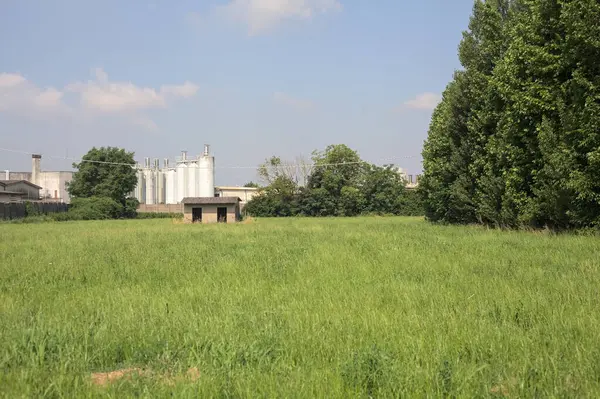 İtalya kırsalında güneşli bir günde arka planda sanayi kompleksi olan terk edilmiş beton bir kulübede terk edilmiş.