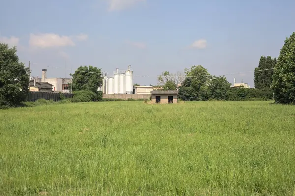 İtalya kırsalında güneşli bir günde arka planda sanayi kompleksi olan terk edilmiş beton bir kulübede terk edilmiş.