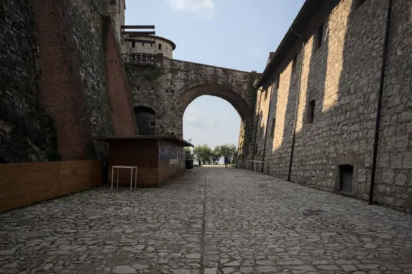 Arka planda kemer olan bir şatoda duvarla taş bina arasında bir patika var.