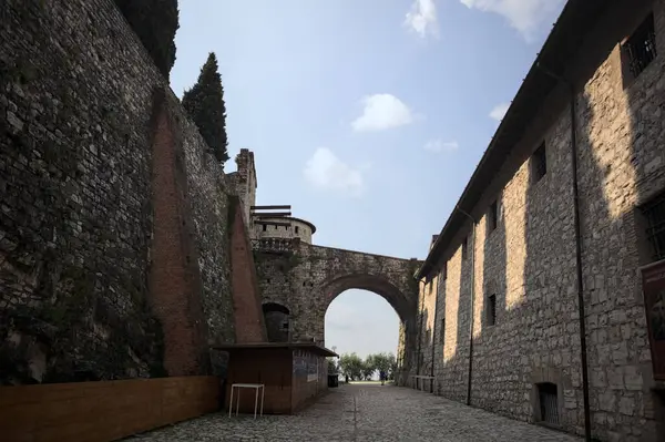 Arka planda kemer olan bir şatoda duvarla taş bina arasında bir patika var.