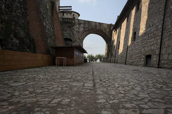 Arka planda kemer olan bir şatoda duvarla taş bina arasında bir patika var.