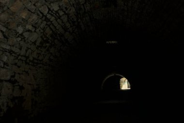 Karanlıkta kemer geçidi, güneş ışığı deliklerden geçiyor ve uzaklarda bir açıklık var.