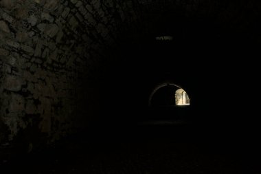 Karanlıkta kemer geçidi, güneş ışığı deliklerden geçiyor ve uzaklarda bir açıklık var.